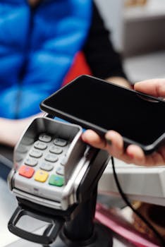 Close-up of a hand making contactless payment using a smartphone at a card terminal.