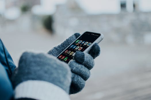 Close-up of hands using smartphone with gloves in winter, showing apps on screen.