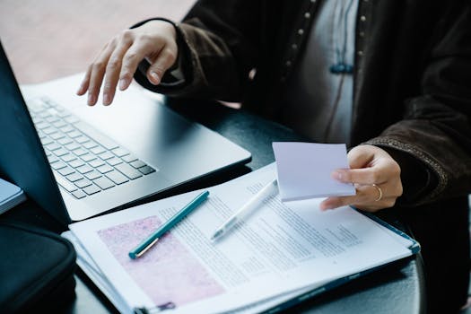 Close-up of a person working with a laptop, documents, and a pen on a desk.